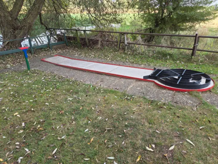 Labyrinthbahn mit schwarzer Spirale direkt am Wasser unter Weiden