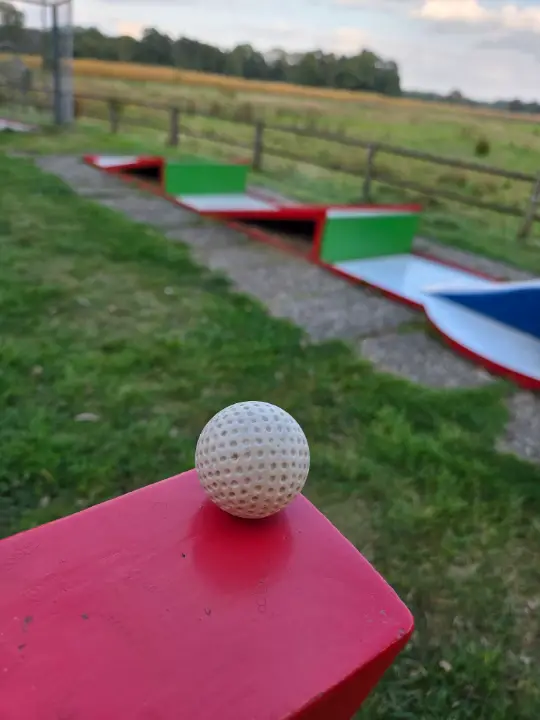 Minigolfball auf einem roten Bahnenschild, im Hintergrund die Bahnen